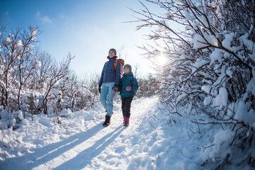 Fototapeta na wymiar A child with a backpack walks with mother in a snowy forest