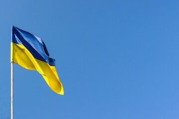 Fototapeta premium Ukrainian national flag flutters in the wind against the blue sky