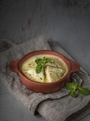 food photography of Georgian traditional dish Gebjalia side view, suluguni cheese in milk with mint leaves and spices on gray textured background close up