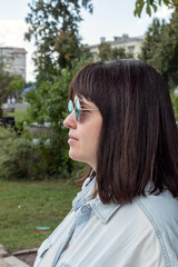 Close-up portrait of a young woman in round sunglasses, in light clothes on a clear, warm day in a city park. Weekend rest. Selective focus.