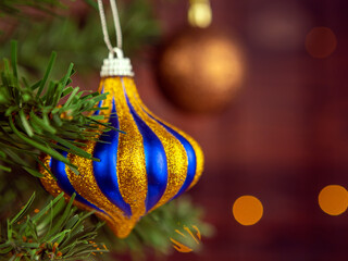 Striped Christmas ball with sparkles on the Christmas tree. Blurred background of garlands.