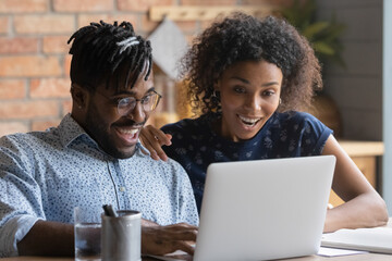 Overjoyed young biracial couple look at laptop screen surprised by good email letter or lottery...