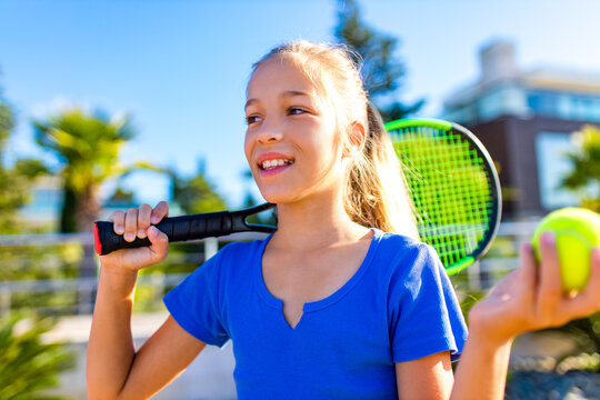 Portrait of a young girl with a tennis racket and ball outdoors tropical background