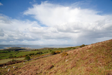 Fototapeta na wymiar Beautiful Welsh countryside overlooking the north Gower coastline with blue skies, white clouds and sporadic rain.