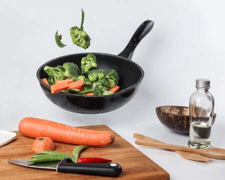 Chopped Sliced Diced Carrot Broccoli White Button Mushroom Red Chili Flying Dropping Gravity Defying On Floating Elevated Metal Frying Pan Cooking Board Bowl Oil Knife On White Background