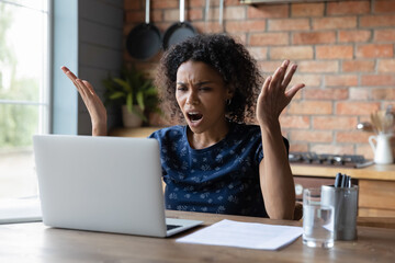 Angry young African American woman look at laptop screen distressed with slow internet connection. Mad biracial female frustrated by computer problem or spam working on gadget at home office. - Powered by Adobe