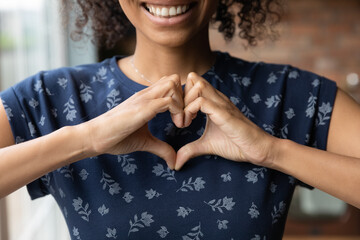 Crop close up of happy African American woman feel grateful thankful show heart sign spread love and care. Smiling biracial female volunteer make hand gesture support ill sick people patients. - Powered by Adobe