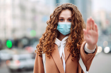 Hand stop sign. Young woman in protective sterile medical mask shows stop hands gesture for stop coronavirus outbreak in quarantine city. Coronavirus, COVID-19.