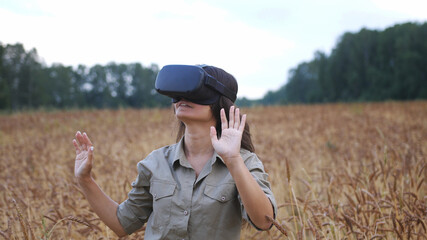 Beautiful girl in a golden wheat field uses virtual reality glasses