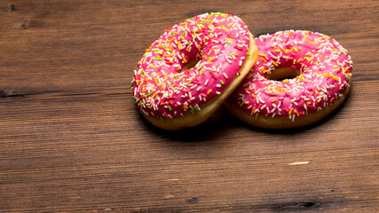 Glazed doughnuts with pink icing with sprinkles on a wooden Board,space for text