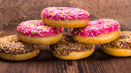Glazed doughnuts with pink chocolate icing with sprinkles on a wooden background,space for text