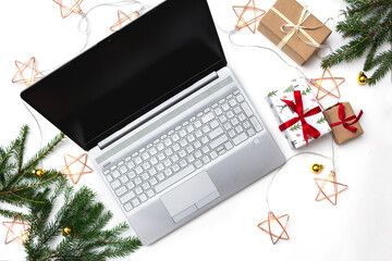 Christmas online shopping. An open laptop on a white background, gift boxes tied with a red ribbon, green fir branches, garlands of stars. Online trading during the winter holidays