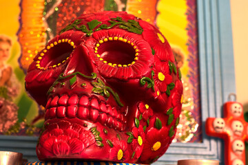 Mexican day of the dead skull with red and green daisies and red teeth, with small red candles