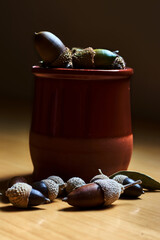 Clay bowl filled with acorns, brown and green, and surrounded by more acorns