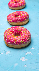 Glazed doughnuts with pink and chocolate icing with sprinkles on a blue background,space for text, close - up