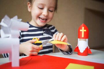 paper craft for kids. DIY toy Saint Nicholas and white horse for sinterklaas day. create art for children. girl cuts paper