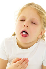 A little girl in a clean white T-shirt swallows a pill, the pill lies on her tongue. Covid-19 concept, virus, disease, treatment.