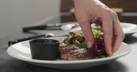 Man put salad next to ribeye steak on a white plate on concrete countertop