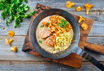 Modern style traditional barbecue pork filet medaillons in cream sauce with chanterelle mushrooms and spaetzle offered as top view on a rustic wrought iron skillet - obrazy, fototapety, plakaty