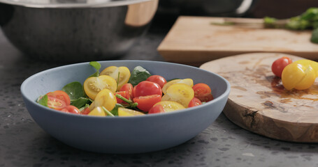 Closeup making salad with spinach, tomatoes and mozzarella in ablue bowl on concrete countertop