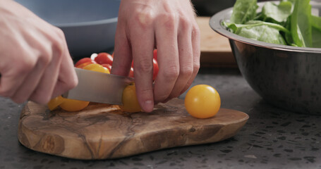 Fototapeta na wymiar man cuts yellow cherry tomatoes on olive wood board