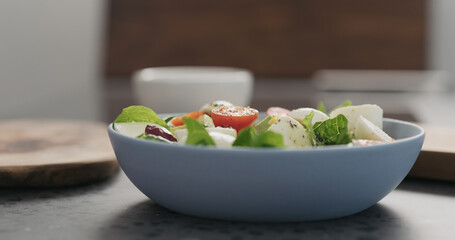 spices fall to salad with mozzarella and mixed salad leaves in a blue bowl on concrete countertop