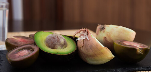 vegetables black tomatoes, avocado and onions on black stone board