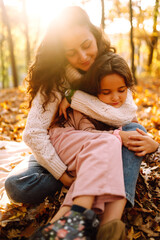 Young Mother and daughter  having fun together in the autumn forest. Mom and child embrace at sunset. Rest on autumn park.