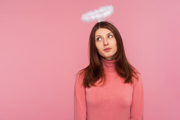 Adorable cute brunette woman in pink sweater standing with halo over head, angelic innocent...