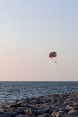 Parasailing in Dubai - single colorful parasail (parachute) tendem wing flying, towed behind a boat before sunset with orange and blue sky background. Copy space, portrait view.