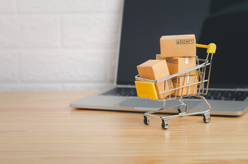 Online shopping and delivery service concept.Brown paper boxs in a shopping cart with laptop on wood table in office background.Easy shopping with finger tips for consumers.
