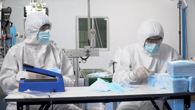 Group of two packer worker wearing ppe suite, face protective mask and glove checking quality , Counting and packing mask on production line of manufacturing  at lab in industry factory