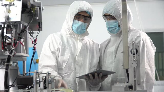 Group of engineer worker wearing ppe suite, face protective mask, glove useing digital tablet analyze  operation and check quality, Maintenance of mask manufacturing machine at lab in industry factory