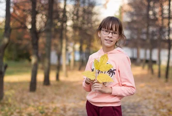 Fotobehang Schattig meisje glimlacht. De tiener houdt een armvol bladeren vast in het herfstpark. © Albert Ziganshin