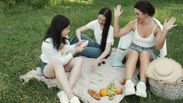 Group of young women sitting on a picnic blanket, having fun while playing cards in a park. Friendship concept