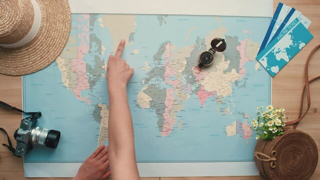 Horizontal from above flat lay shot of female hands pointing places on world map for travelling