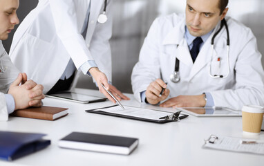 Group of unknown doctors are sitting at the desk and discussing medical treatment, using a clipboard, close-up. Team of physicians at work in a clinic. Medicine and healthcare concept