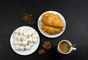 Coffee, chocolate, croissants and marshmallows on a dark background. Top view