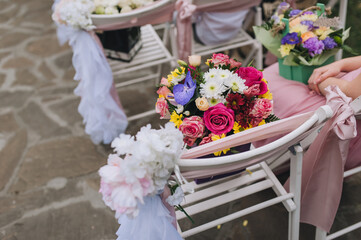 A paper basket with yellow, white, red and purple flowers stands on decorated wooden chairs for a wedding ceremony. Photography, concept.
