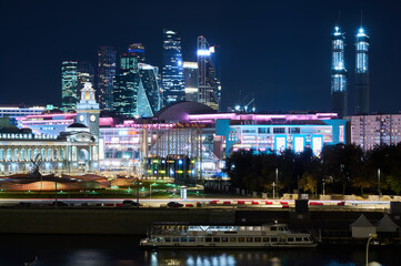 Fototapeta premium Moscow at night, sparkling with bright lights with a river and boat in the foreground and sparkling skyscrapers in the background