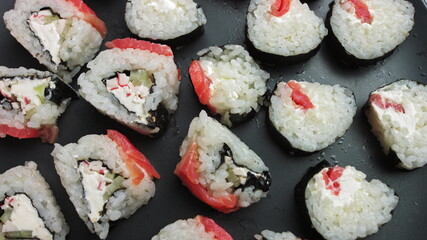 Various kinds of sushi served on a dark background.Sushi rotate.Macro set of fresh Philadelphia sushi from fish, salmon, rice, cucumber. Sushi restaurant, sushi delivery.