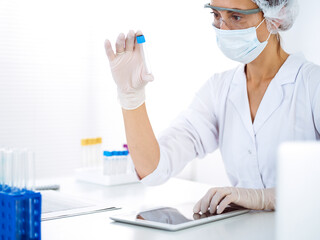Professional female scientist in protective eyeglasses researching tube with reagents in...
