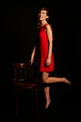 Young brunette Spanish woman dressed in sexy red dress, matching beaded earrings, and black shoes on black background,red
