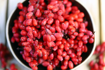Berries and bunches of barberry in a bowl on a wooden surface. Barberry.