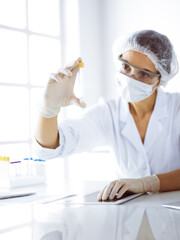 Professional female scientist in protective eyeglasses researching tube with reagents in laboratory. Concepts of medicine and science researching