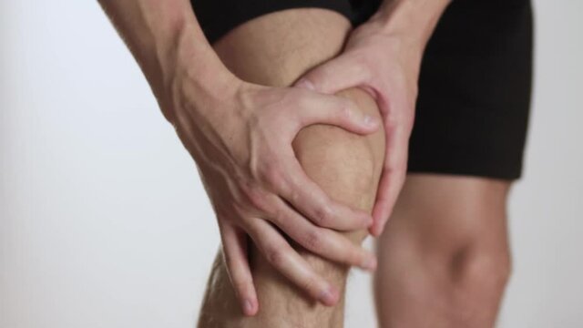 The man has a sore knee, pain in the leg. Close up. Isolated on a gray background.