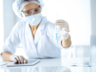 Professional female scientist in protective eyeglasses researching tube with reagents in...