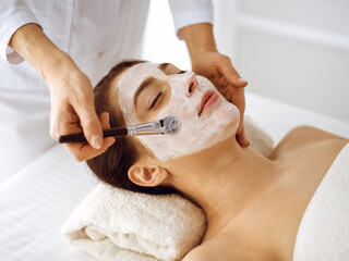 Beautiful brunette woman enjoying applying cosmetic mask with closed eyes. Relaxing treatment in medicine and spa center concepts