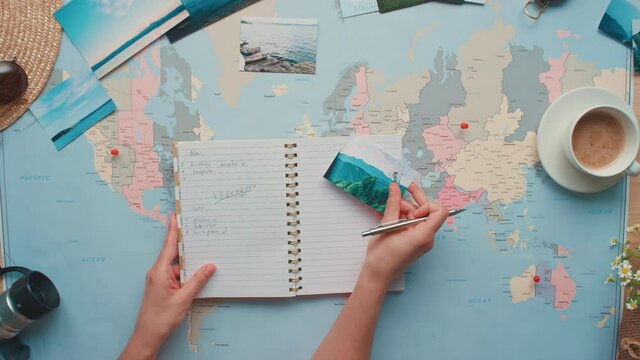 Top view flat lay shot of woman opening notebook lying on world map and writing notes for travelling inside