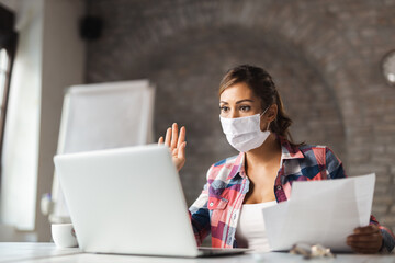 Young businesswoman wears mask while having a video conference call with someone over the computer in the office